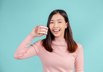 Fototapeta premium Dental of asian woman with tooth sample and white teeth increase confidence for healthy on blue background isolated studio shot, Happiness teenager smiling facial expression.