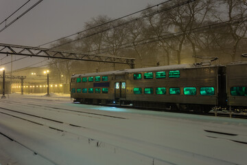 Fototapeta na wymiar Large passenger train car with green windows at rest in the snow on overcast night in urban Chicago