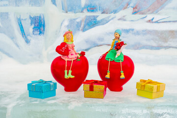 Toys, a couple in love, a guy and a girl, sit on red hearts with objects in their hands on an abstract ice background. There are boxes with gifts below. Valentine's Day