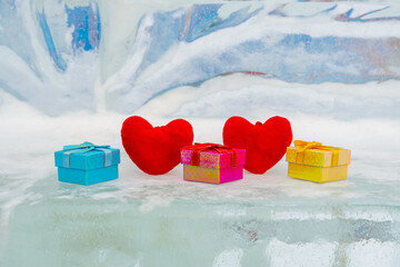 Two red hearts and multi-colored boxes for gifts lie on an abstract ice background, valentine's day