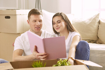 Portrait of happy couple looking at laptop computer together sitting in new house, surrounded with boxes