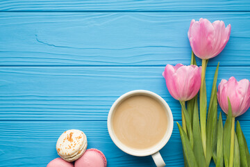 Top overhead view photo of pastel color tulips with cup of latte tasty delicious macarons on blue bright table with empty blank space