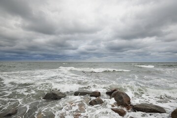 Dark storm clouds above the Baltic sea. Kiel, Germany. Rocks, waves and water splashes close-up. A view from the pier. Fickle weather, climate themes. Nature, tourism, cruise, recreation