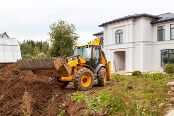 Fototapeta na wymiar yellow bucket excavator levels pile of earth in front of country cottage