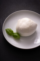 dish with typical Italian mozzarella and basil leaves, on dark stone background