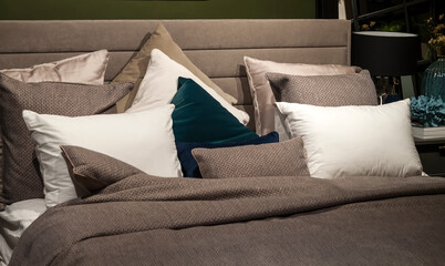Close-up of new brown colored blanket with decorative pillows, fabric headboard in bedroom in sample model of hotel or apartment
