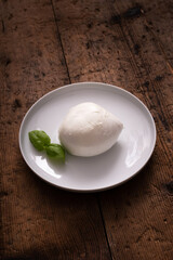 dish with typical Italian mozzarella and basil leaves, on wooden table