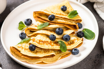Crepes with blueberries and honey at kitchen table. Healthy breakfast or snack.