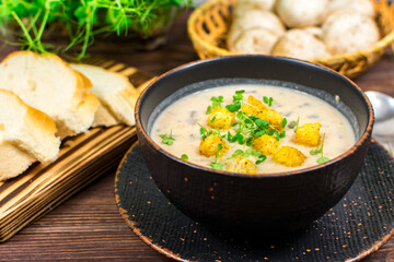 A bowl of homemade mushroom puree soup with herbs and bread on a wooden table. Homemade vegetarian mushroom soup with vegetables and bread.