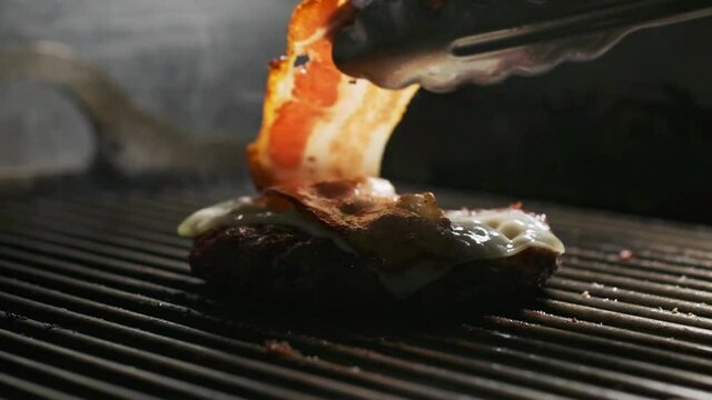 Video of young hand's chef preparing delicious burger on grilled while putting cheese and bacon in the restaurant kitchen.