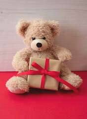 Teddy bear holding a gift box sitting on red floor. Valentines day.