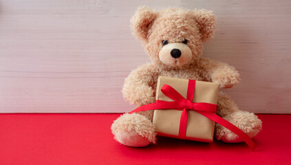 Teddy bear holding a gift box sitting on red floor. Valentines day.