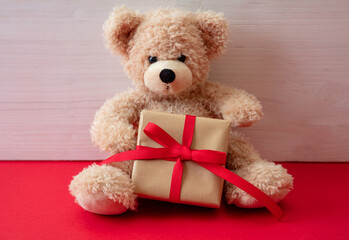 Teddy bear holding a gift box sitting on red floor. Valentines day.