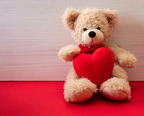 Teddy bear holding a red heart sitting on red floor. Valentines day.