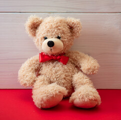 Teddy bear with a red bow tie sitting on red floor. Valentines day.
