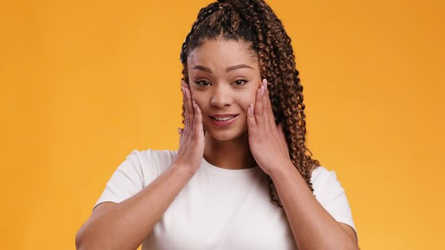 Close up portrait of funny african american woman touching her cheeks in shock and saying OMG, orange background
