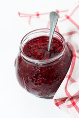 jar with sweet cowberry jam on white table, vertical