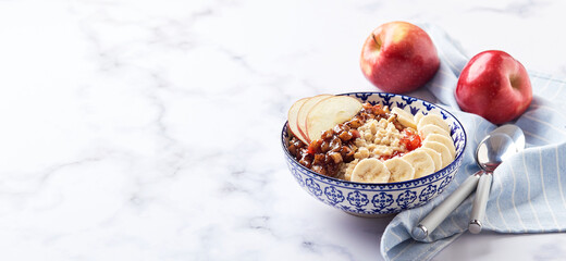 Oatmeal porridge with caramelized apples with cinnamon, banana, grated strawberries and honey on light marble background