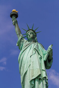A vertical image of the Statue of Liberty in New York with the blue sky in the background on a sunny day