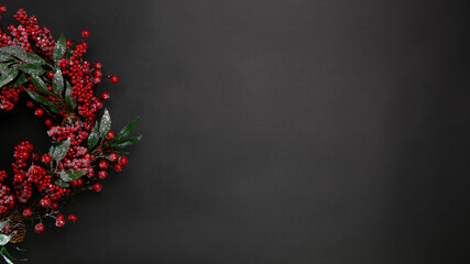 Christmas wreath decorated with red, vibrant berries and pine cones. View from above. Black background
