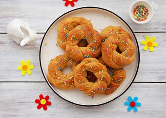 Traditional buttery twisted Italian Easter cookies with multicolored sugar decor on a white plate on a white wooden background. Easter sweets.