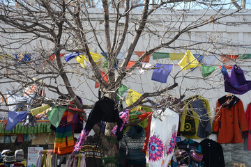 Brightly colored clothes, hats, shirts, scarves, and bunting hanging on a tree.