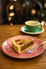 A vertical photo of a piece of a pecan pie on a plate and a cup of coffee, bokeh lights in the background, selective focus