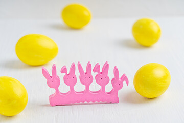 Pink silhouette of easter rabbits surrounded by boiled eggs colored or dyed in vibrant yellow color prepared for easter celebration party laying on white wooden table. Horizontal orientation image
