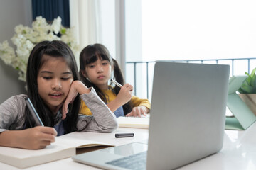 Little Asian girl studying online lesson at home with sister. Homeschooling during quarantine online education concept.