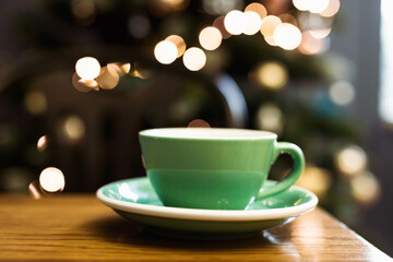 Obraz na płótnie Canvas A horizontal lifestyle photo of a green cup of black coffee on a saucer, a spoon, bokeh lights in the background, selective focus