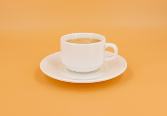 White cup with coffee on orange background