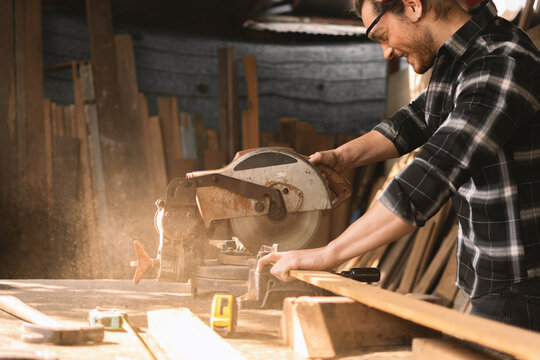 Carpenter Wearing Googles Using A Chop Saw To Cut Wood Plank On The Table Work With Measure Tape At Sawmill.