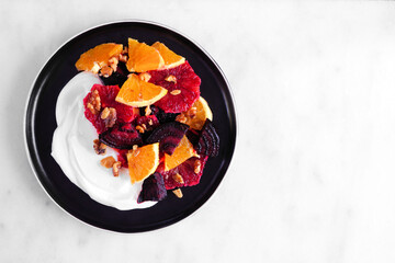 Yogurt with colorful oranges, blood oranges, beets and walnuts. Health eating concept. Top down view on a bright background.