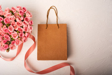 Bouquet of pink roses in the shape of a heart with a gift in a craft bag on a light background