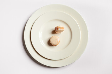 Two light macaroons in a light plate on a light background, minimalist composition, top view