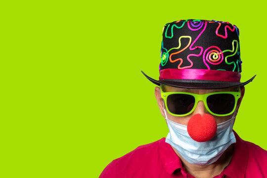 Man in corona und covid 19 times at carnival with red clown nose, sun glasses and yellow background, copy space