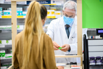 Senior pharmacist dealing with a customer, both of them wearing masks due to coronavirus