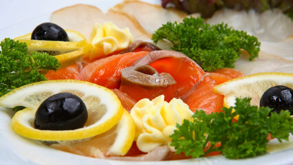 Sliced fish assortment with herds and lemon on white oval plate