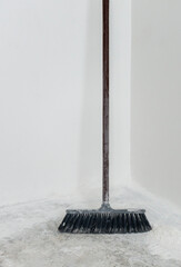 Dirty dusty old broom on the grunge floor in the corner of a renovated room 
