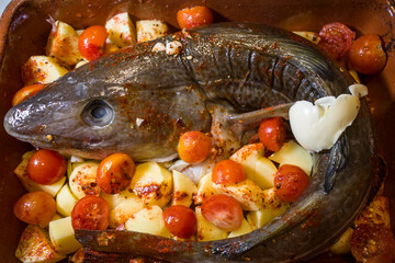A whole Baltic Sea pike in a baking dish with potatoes, tomatoes, salt, pepper, butter, garlic and paprika