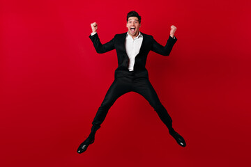 Fototapeta na wymiar Excited european man jumping in valentine's day. Studio shot of male model in suit dancing and smiling.