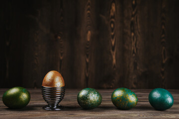 Shiny green and gold Easter eggs on a brown wooden background.