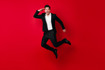 Inspired caucasian guy jumping in studio. Brunette man in black suit fooling around.