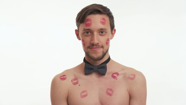 Attractive American half naked brunette man says some phrase and winks with his right eye isolated on white wall background. Body of guy covered with lipstick kiss marks, looks like stripper dancer.