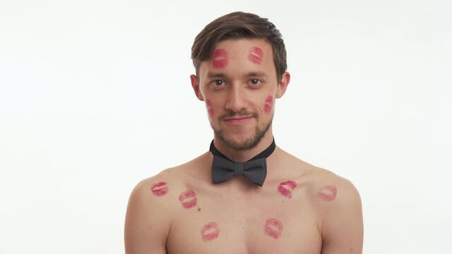 Young nice guy with grey bow tie flirt, raises his eyebrows. Concept of Valentine's day close up. Attractive lovely man with kiss imprints or marks look at the camera isolated on white wall background