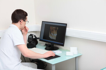 Fototapeta na wymiar Dentist doctor examines images of teeth on a computer screen. Modern dentistry. Volumetric image. Photo camera on the desktop. Photo in the interior.