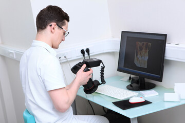 The dentist holds a camera with a ring flash in his hands. The work of a doctor in a dentistry office. Images of teeth on a computer screen. Modern dentistry. Volumetric image.