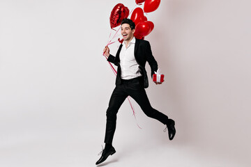 Full length view of brunette man dancing with heart balloons. Studio shot of happy boy isolated on white.