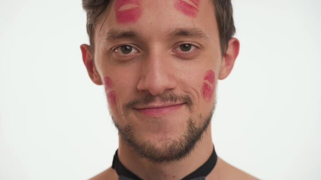 One lovely young Caucasian bearded brunette man, kissed by girlfriend with lipstick kiss marks on face, cheek smile, flirt isolated on white background. Romantic concept of Happy Valentines day.