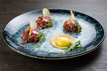 beef tartare with egg, white bread croutons and fresh radish. scrambled eggs with glaze. on a blue marble plate